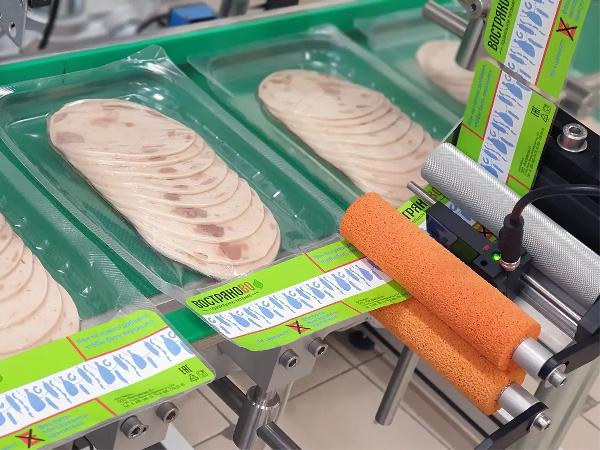 Novexx — 1-позиционное верхнее нанесение этикетки на пищевые лотки с продуктами на конвейерной линии