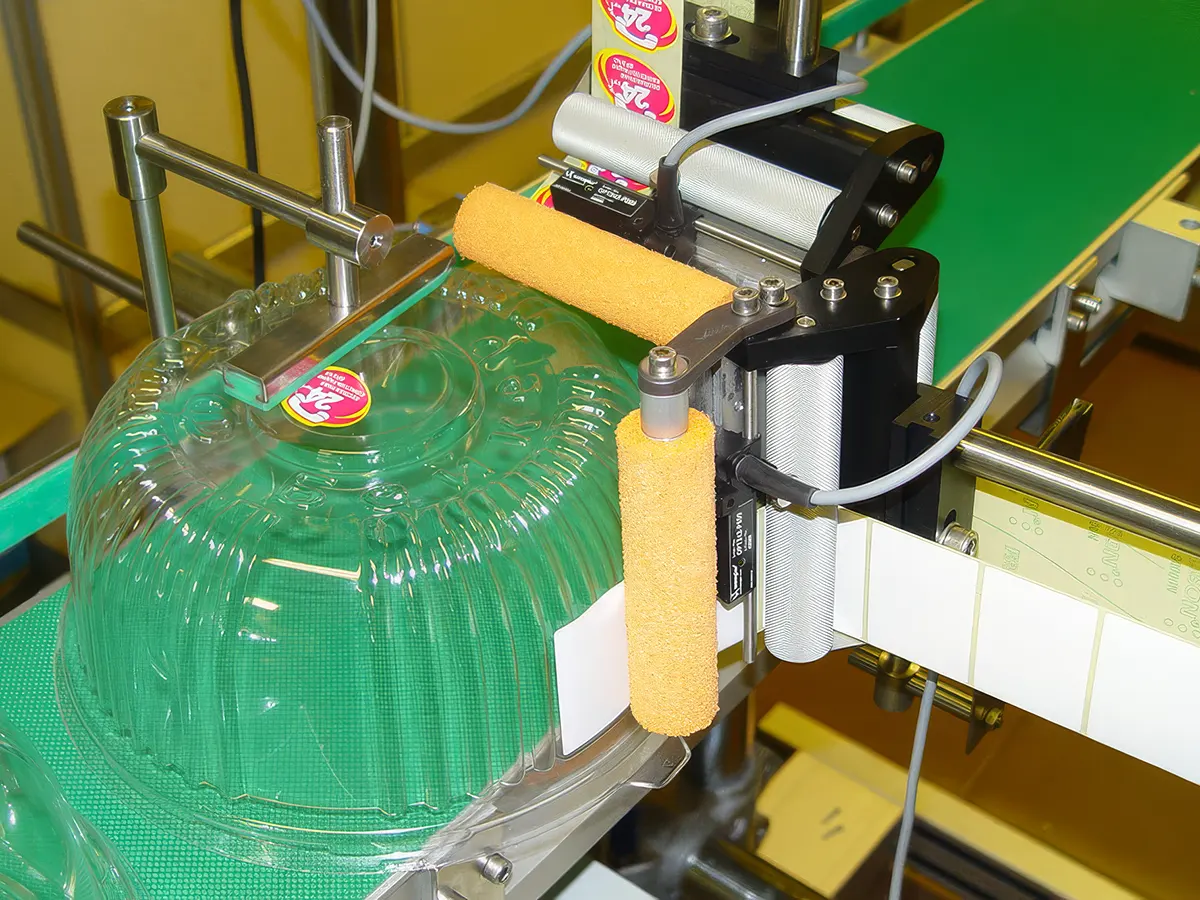 Novexx — 2-позиционное боковое и верхнее этикетирование круглой пластиковой упаковки для торта на конвейерной линии